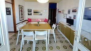 A dining area with a table, chairs, a vase of flowers, and a television. - Spacious Beachfront Apartment With Terrace (San Michele al Tagliamento)