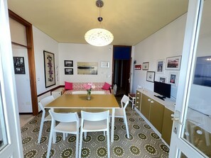 A dining area with a table, chairs, a vase of flowers, and a television. - Spacious Beachfront Apartment With Terrace (San Michele al Tagliamento)