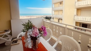 A balcony with a view of the beach, a table with chairs, and a vase of flowers. - Spacious Beachfront Apartment With Terrace (San Michele al Tagliamento)