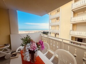 A balcony with a view of the beach, a table with chairs, and a vase of flowers. - Spacious Beachfront Apartment With Terrace (San Michele al Tagliamento)
