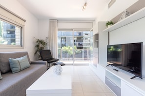 Ein modernes Wohnzimmer mit einer Couch, einem Couchtisch, einem Fernseher und einem Balkon mit Blick auf Gebäude.