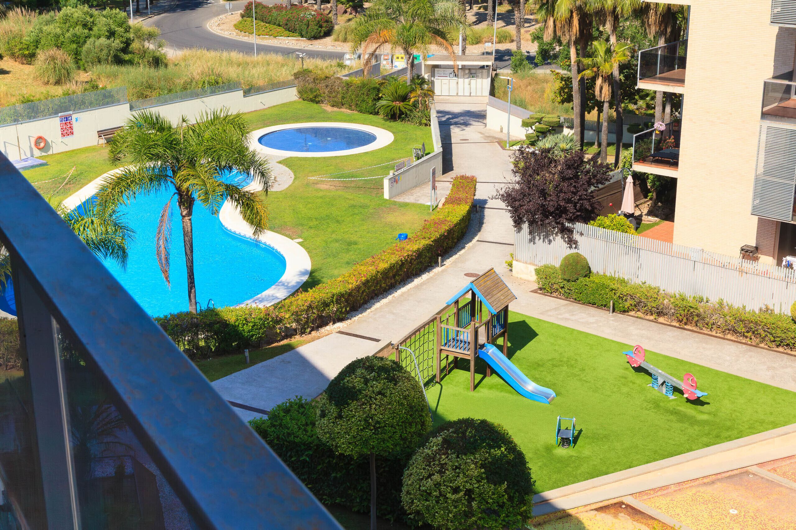 Ein Wohngebiet mit Schwimmbad, Kinderspielplatz und einer Straße im Hintergrund.