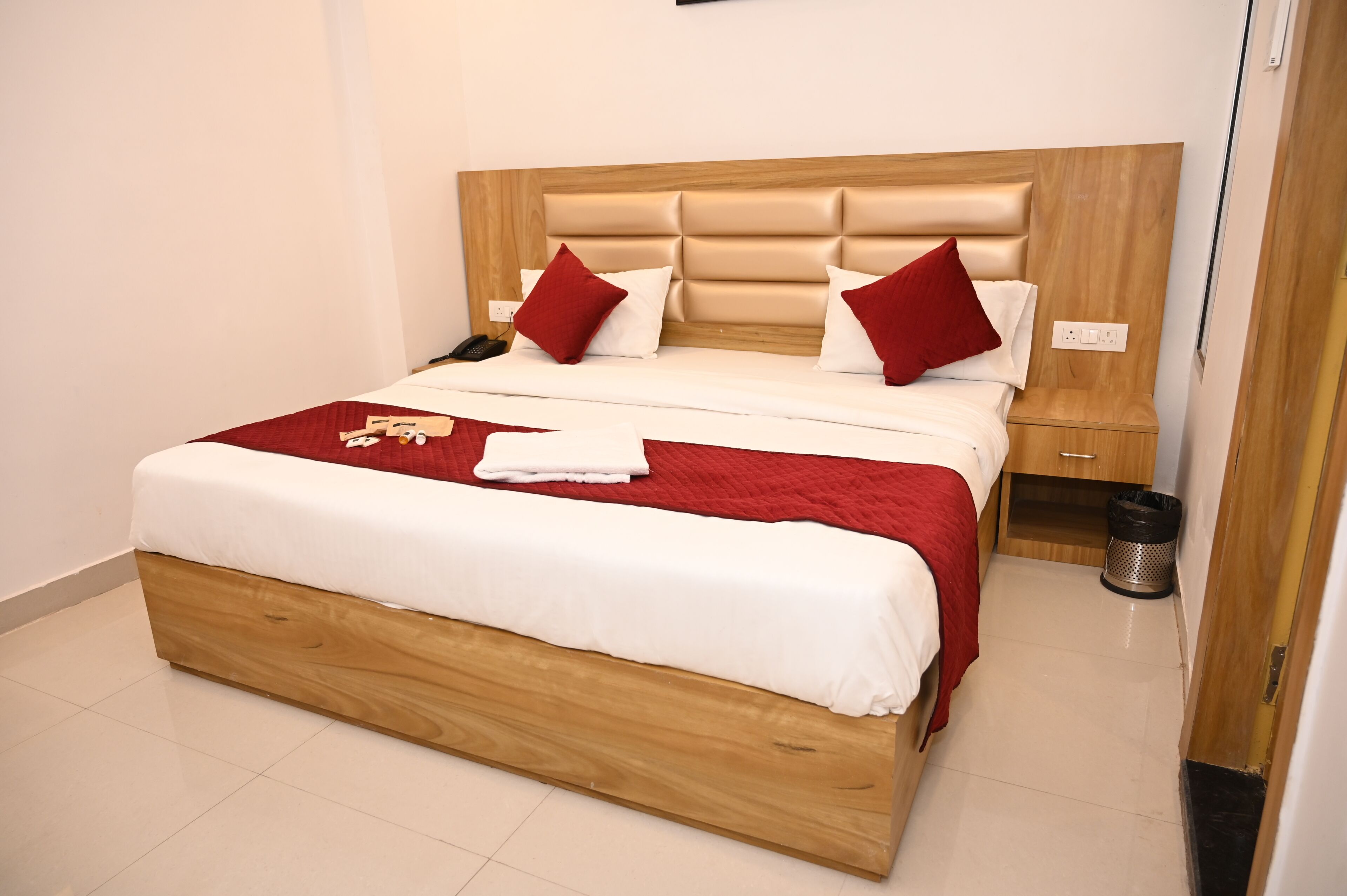 A neatly made bed with a wooden headboard, a bedside table, and a trash bin.
