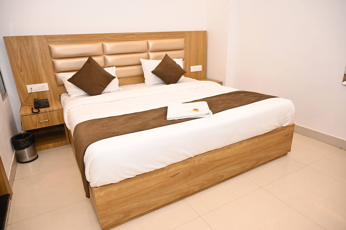 Una cama bien hecha con cabecera de madera, una mesita de noche con un teléfono y un cubo de basura.