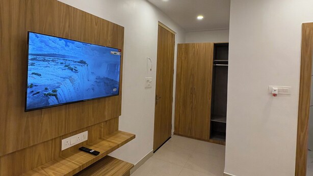 Una sala de estar moderna con un televisor de pantalla plana montado en una pared de madera, un banco de madera, un armario y piso de baldosas.