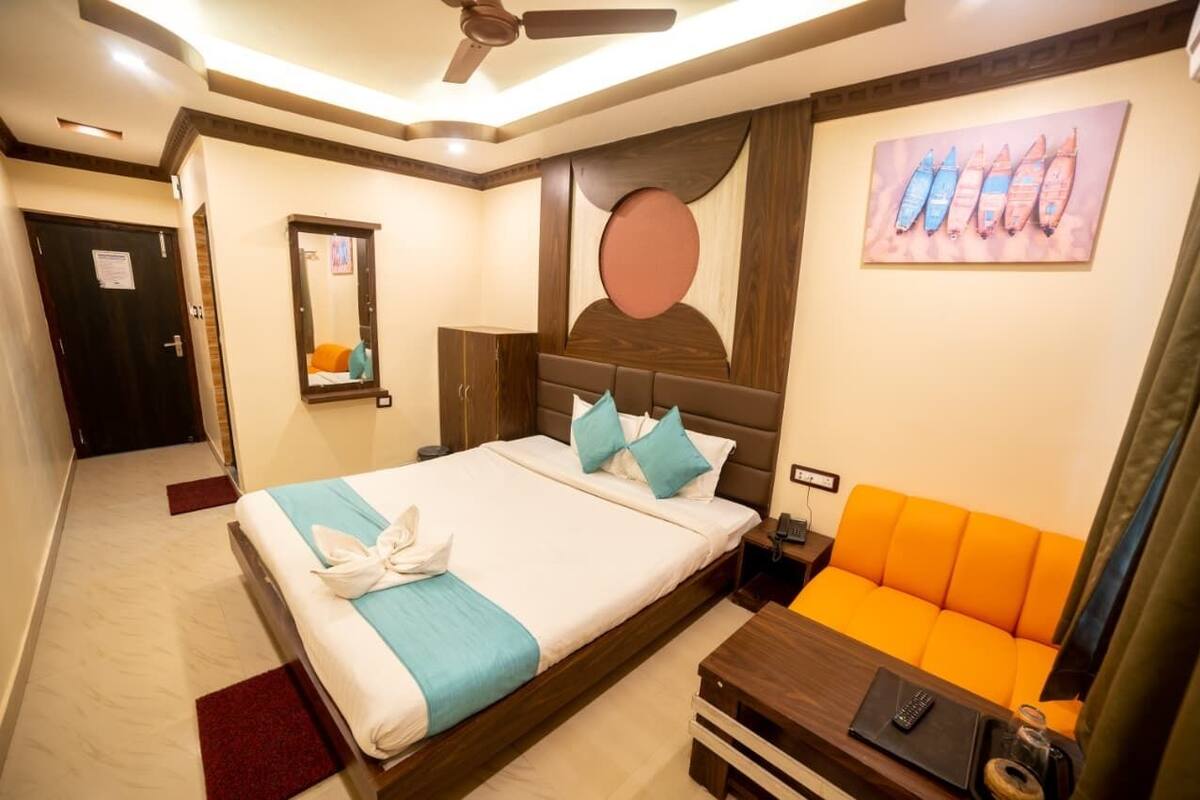 Una habitación de hotel con una cama, una mesita de noche, un sofá, un ventilador de techo, un espejo y un cuadro en la pared.