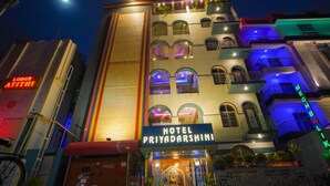 A multi-story hotel with balconies, a prominent sign for 'HOTEL PRIYADARSHINI,' and adjacent buildings with neon signs.
