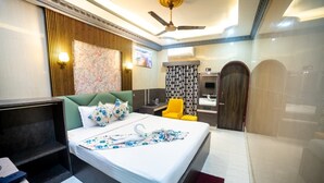 A hotel room with a bed, a desk, a chair, a ceiling fan, and a bathroom with a mirror and a door.