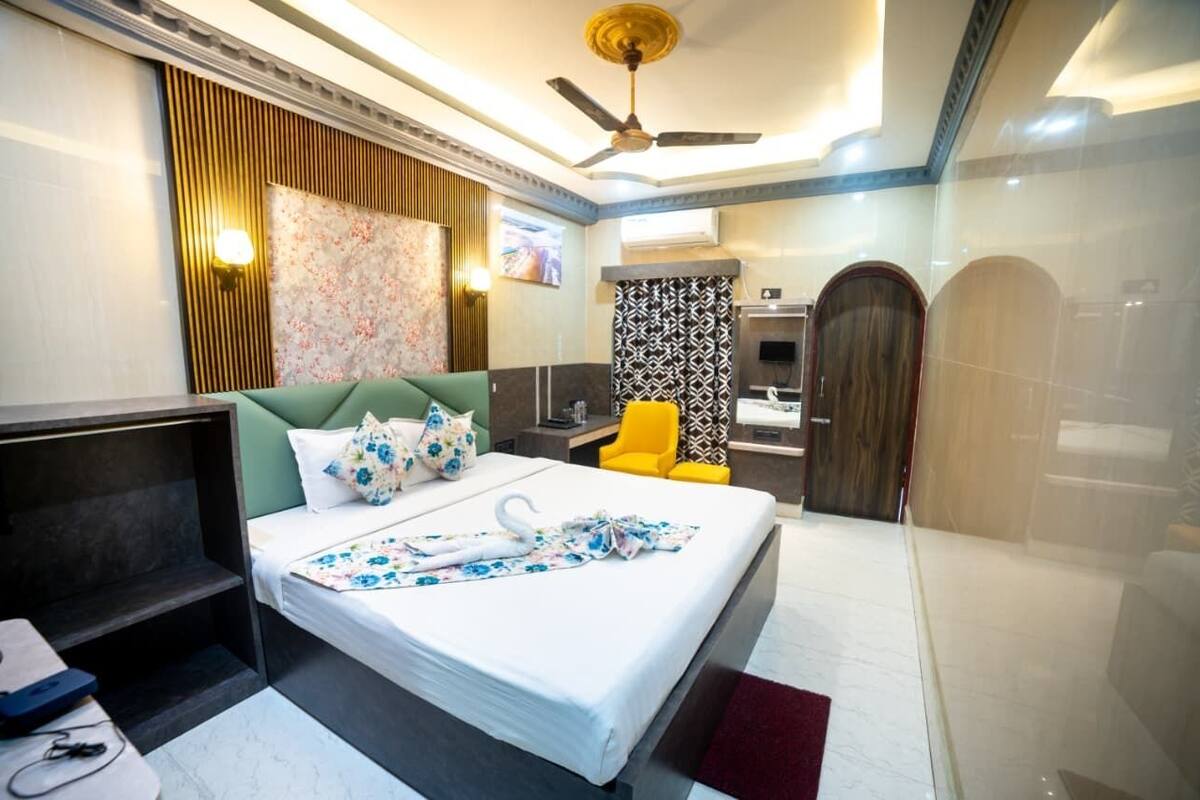 Habitación de hotel con cama, escritorio, silla, ventilador de techo y baño con espejo y puerta.