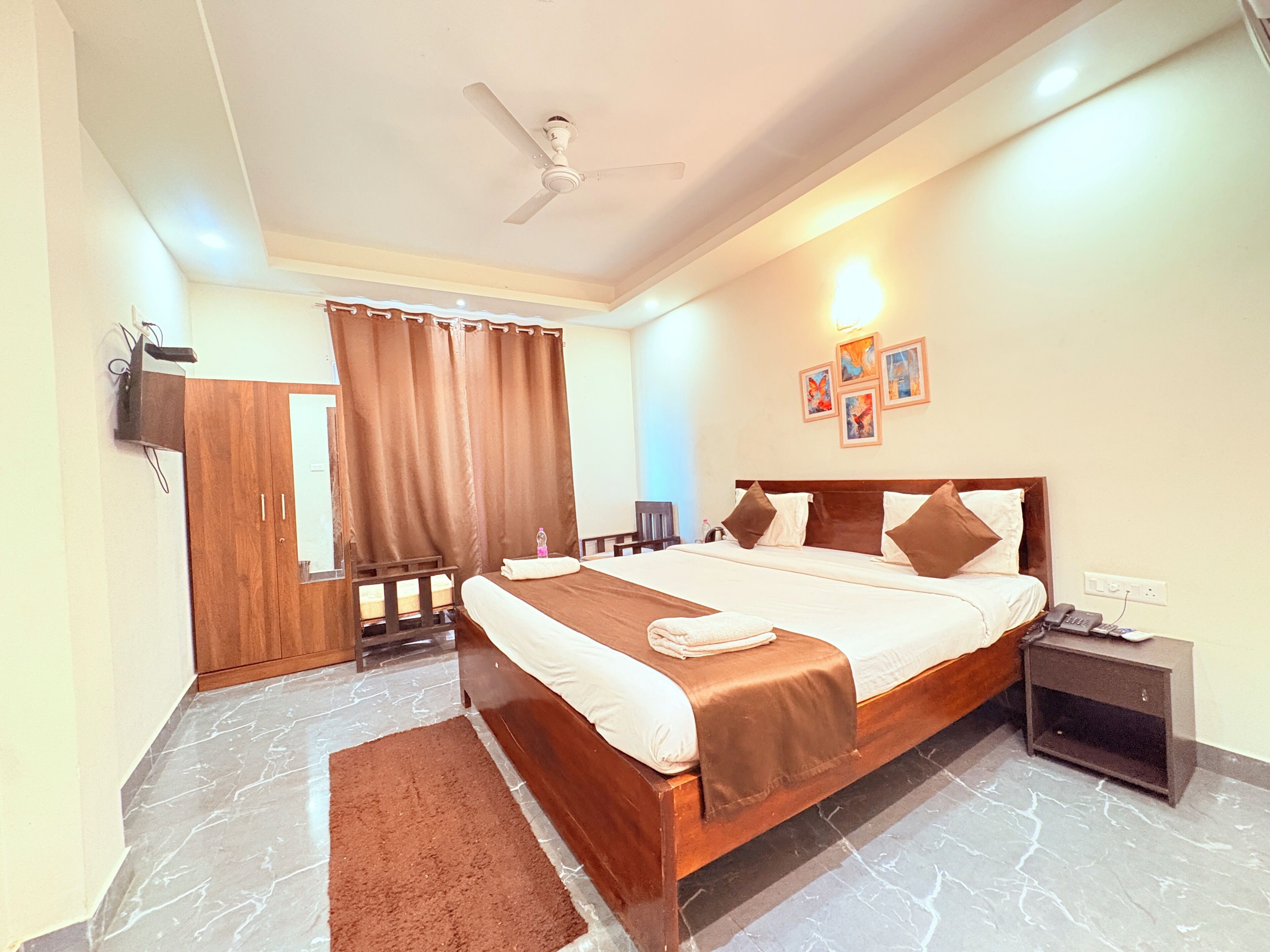 A hotel room with a bed, a ceiling fan, a nightstand, a desk, a wardrobe, and a bathroom.