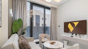 Ein modernes Wohnzimmer mit einer Couch, Sesseln und einem Couchtisch, einem Flachbildfernseher sowie einem Balkon mit Blick auf Gebäude.