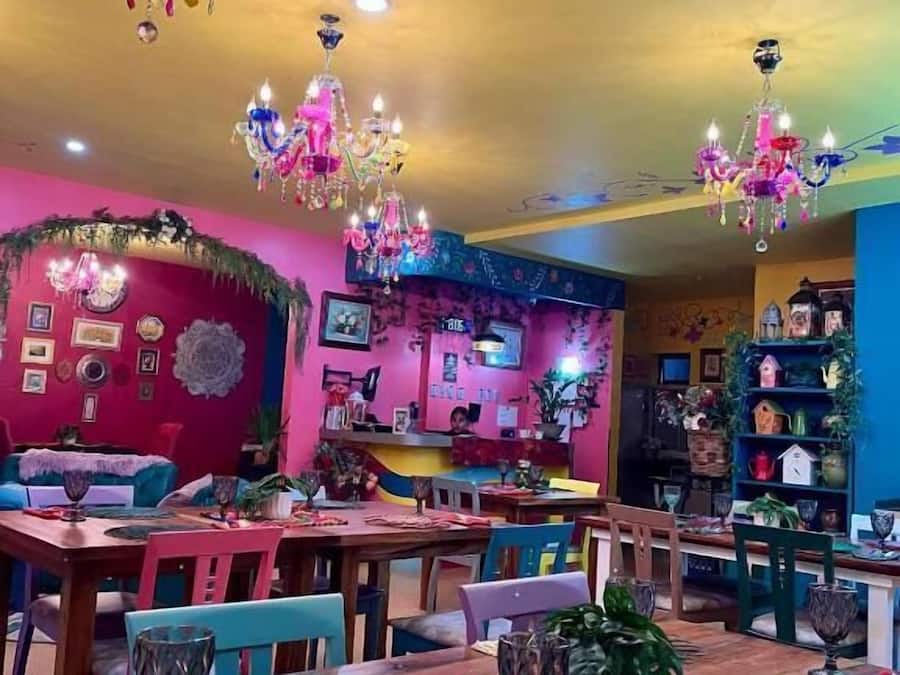 Uma área de refeições vibrante com várias mesas, cadeiras e lustres coloridos.
