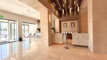 A hotel lobby with a reception desk, marble flooring, and a modern ceiling design.