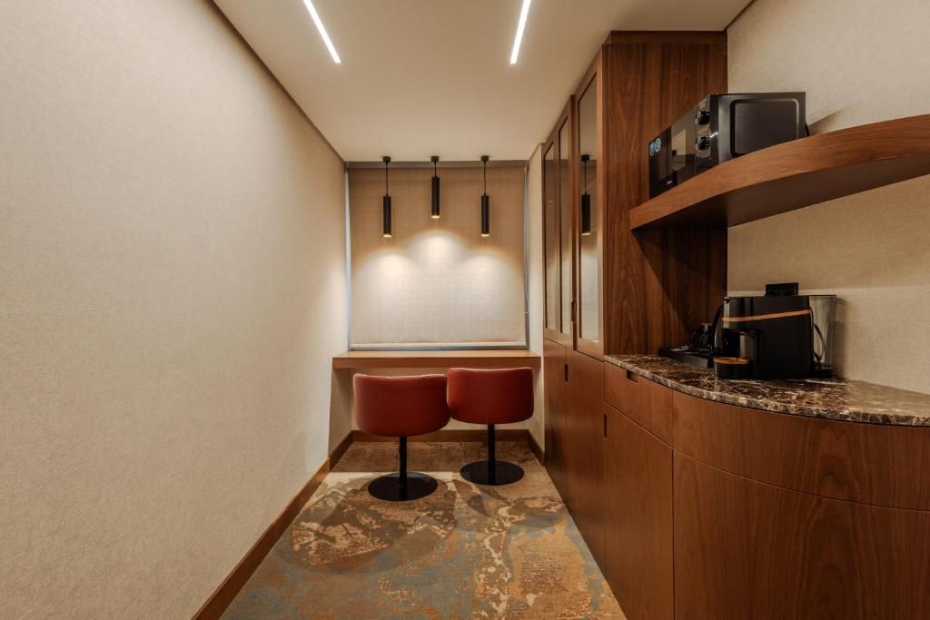 A narrow hallway with a wooden counter, two red stools, and pendant lighting.