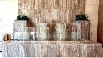 A reception area with a marble wall, a reception desk, and two potted plants.