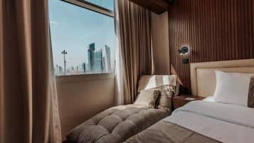 Habitación de hotel con una cama, una mesita de noche, una lámpara y vistas a un horizonte urbano a través de una ventana.