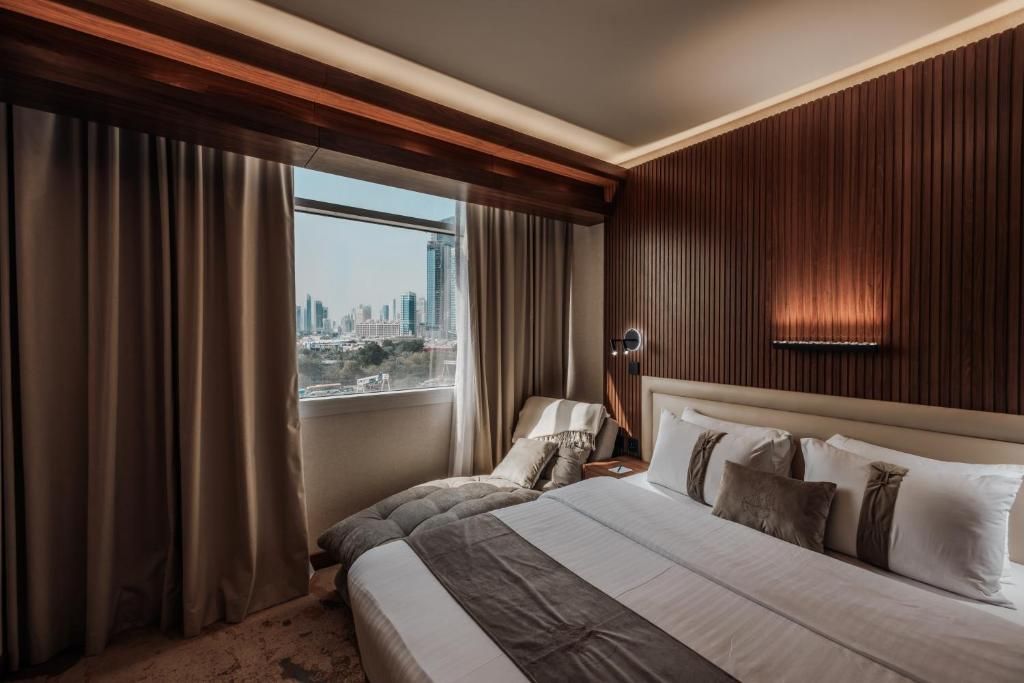 A hotel room with a large bed, a view of a cityscape, and a wooden panel wall.