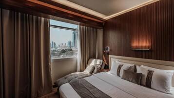 A hotel room with a large bed, a view of a cityscape, and a wooden panel wall.