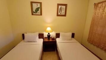 A room with two single beds, a nightstand with a lamp, and two framed botanical prints on the wall.