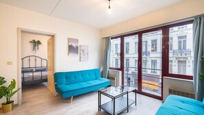 Una sala de estar moderna con un sofá azul, una mesa de centro de vidrio y vistas de la ciudad a través de amplias ventanas.