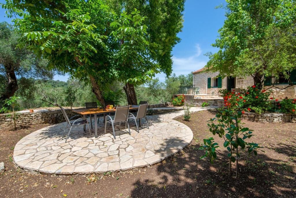 A stone patio with a table and chairs, surrounded by trees and a stone wall.