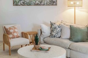 Un salon comprenant une table basse ronde, un canapé, un fauteuil, une petite table d’appoint et un lampadaire.