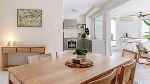 A modern dining area with a wooden table, chairs, a ceiling fan, and a kitchen in the background. - A Calm City Base Cairns CBD (Cairns North)