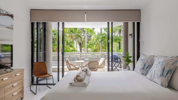 Een slaapkamer met een groot bed, een televisie, een houten dressoir en een balkon met buitenmeubilair.