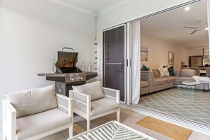 A living room with a grill, white furniture, a sliding glass door to a balcony, and a patterned floor.