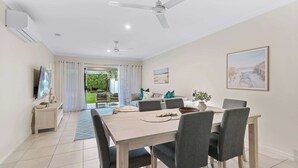 Un espace repas moderne avec une table et des chaises en bois, un téléviseur posé sur un meuble et un tableau accroché au mur.