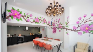 A modern kitchen with black cabinets, a white countertop, and a dining area with a white table and orange chairs.