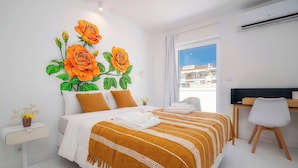 A modern hotel room with a large bed, a desk, and a view of the city through the window.
