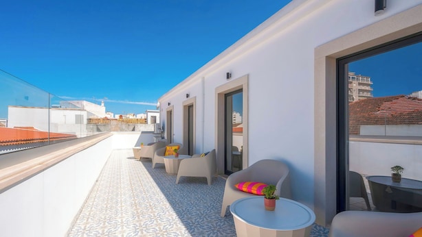 A rooftop terrace with a patterned floor, outdoor seating, and a view of the cityscape.