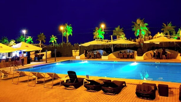 A swimming pool with lounge chairs and umbrellas, surrounded by palm trees and a bar area. - Hotel Anaklia  (Anaklia)