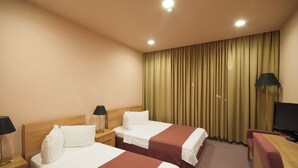 A hotel room with two beds, a TV, a desk, and a large window with curtains. - Hotel Anaklia  (Anaklia)