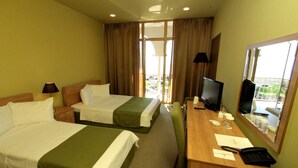 A hotel room with two beds, a desk with a TV, a phone, and a window with a view. - Hotel Anaklia  (Anaklia)