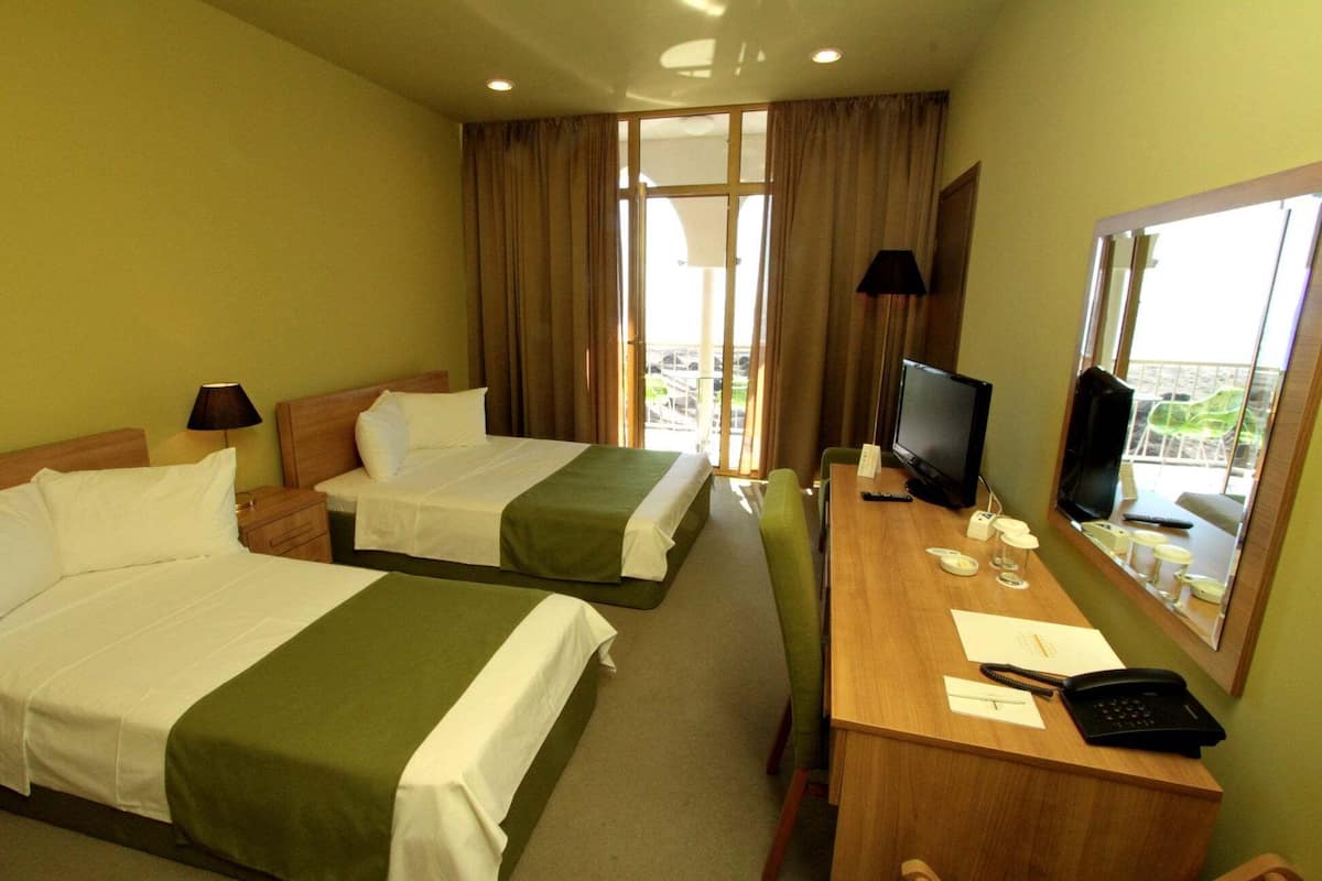 A hotel room with two beds, a desk with a TV, a phone, and a window with a view.