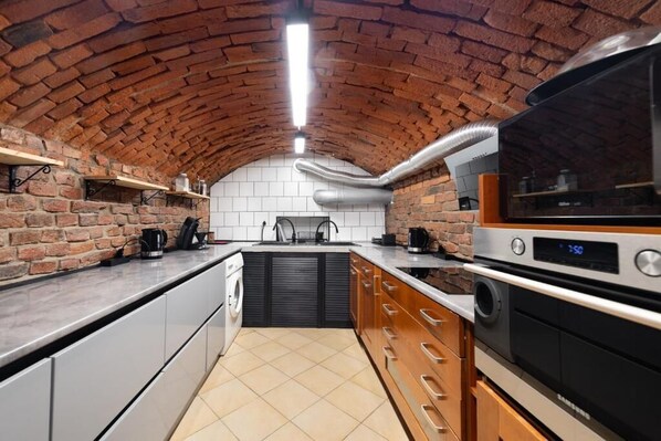 A kitchen with brick walls, a tiled backsplash, stainless steel appliances, and wooden cabinets. - Apart HOSTEL KrakHouse (Kraków)
