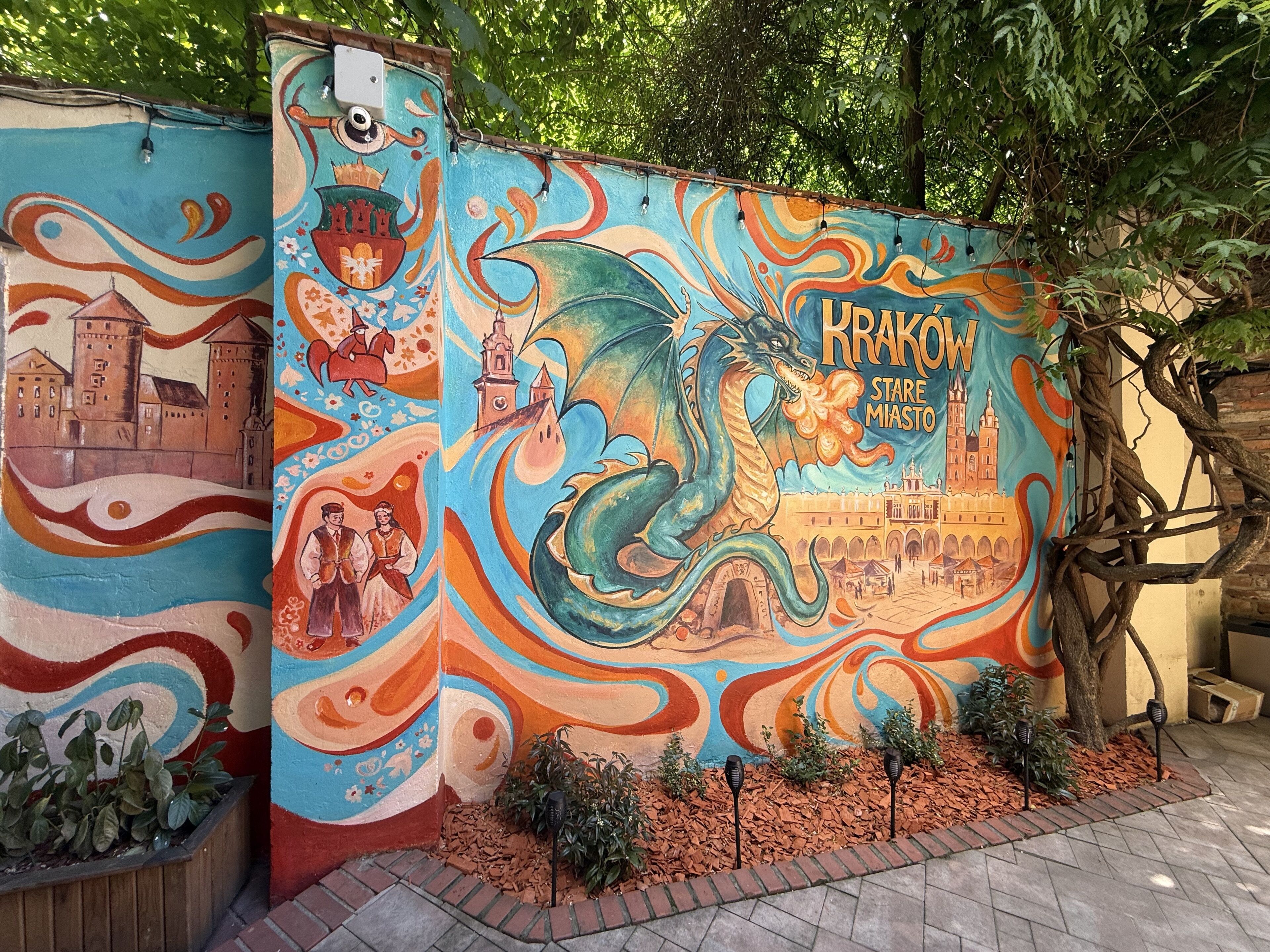 A colorful mural with a dragon and a castle, a tree, and a brick pathway.