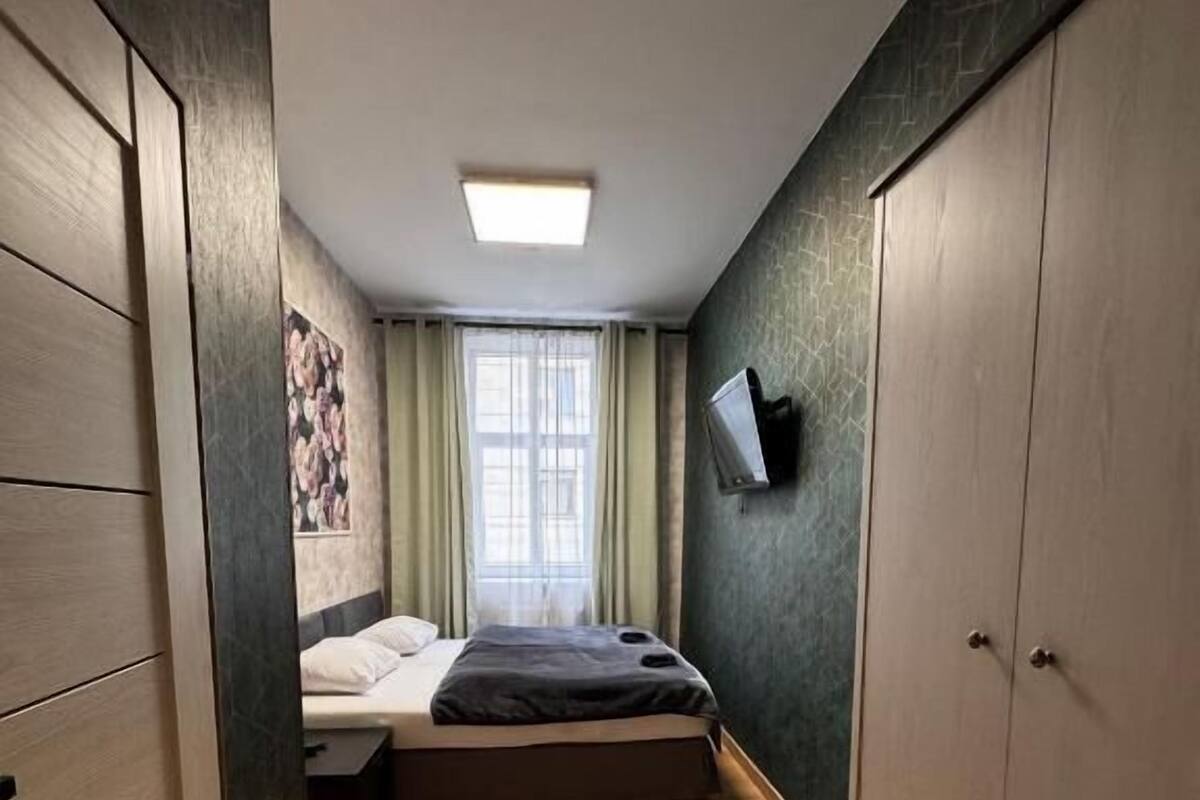 A narrow room with a bed, a TV mounted on the wall, and a wardrobe.