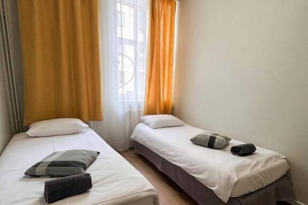 A room with two beds, a window with curtains, and a wooden floor.