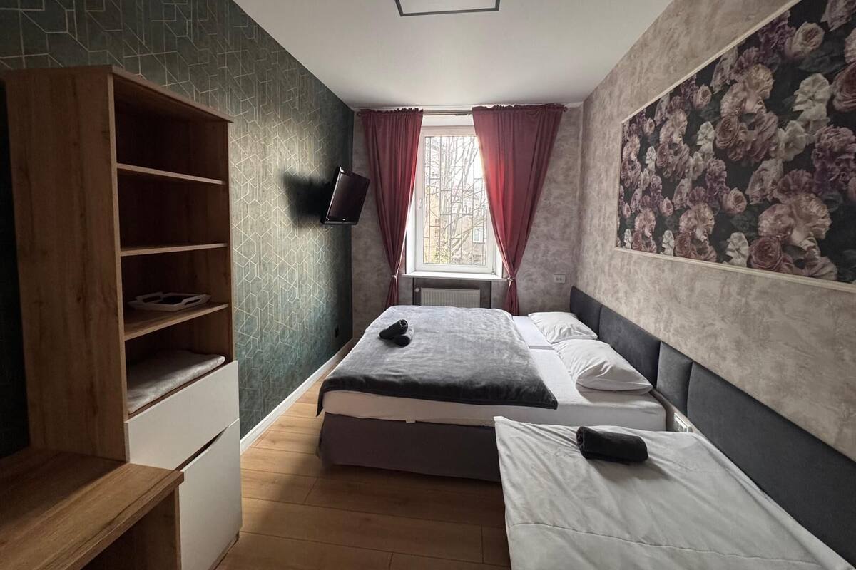 A bedroom with a bed, a TV, a wooden shelf, and a window with curtains.