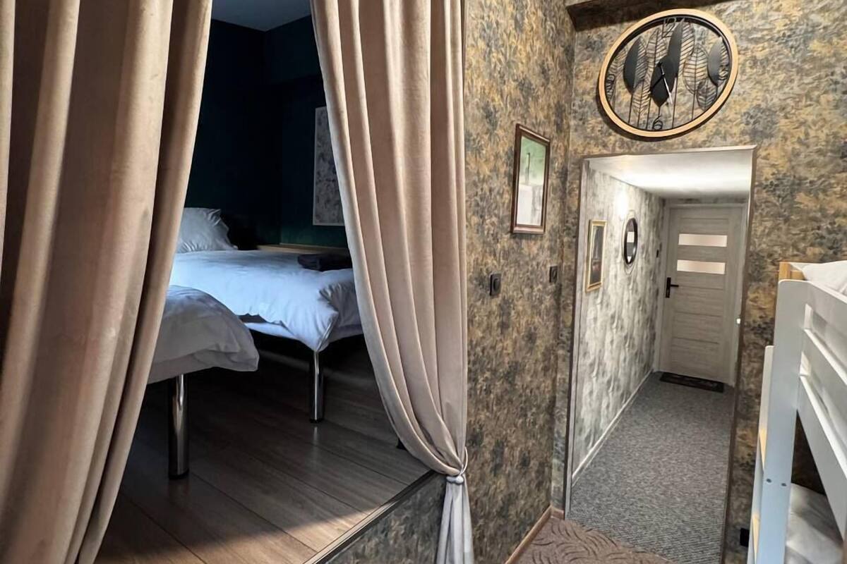 A bedroom with a bed, curtains, a clock, a door, and a staircase.