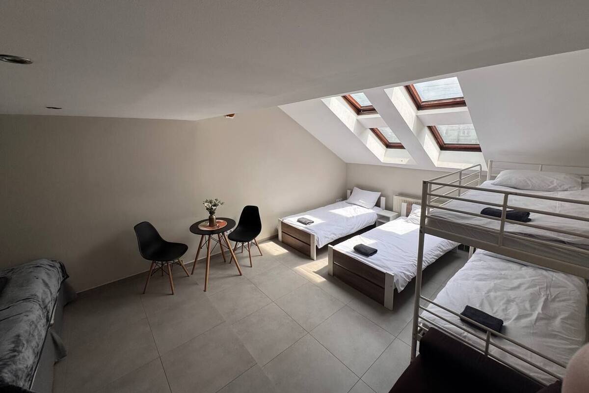 A dormitory room with bunk beds, a desk, two chairs, and skylights.