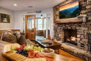 A cozy living room with a stone fireplace, a wooden coffee table, and a fruit platter. - Whispering Waters, Hot Tub, Riverside, Free Tickets (Pigeon Forge)