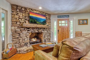 A stone fireplace with a painting above it, a cozy seating area, and a sign on the wall that reads 'This is My Happy Place.' - Whispering Waters, Hot Tub, Riverside, Free Tickets (Pigeon Forge)