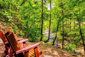 A forested area with a wooden bench and a stream. - Whispering Waters, Hot Tub, Riverside, Free Tickets (Pigeon Forge)
