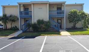 A two-story building with a number '600' on the facade, a parking lot in front, and a tree to the right. - Designer #601 Chateau La Mer II 1st Floor 1-Bd 1 Bath Newly Added Near Pool (Destin)