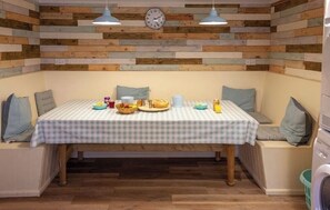 A dining area with a checkered tablecloth, wooden wall paneling, two pendant lights, and a clock.