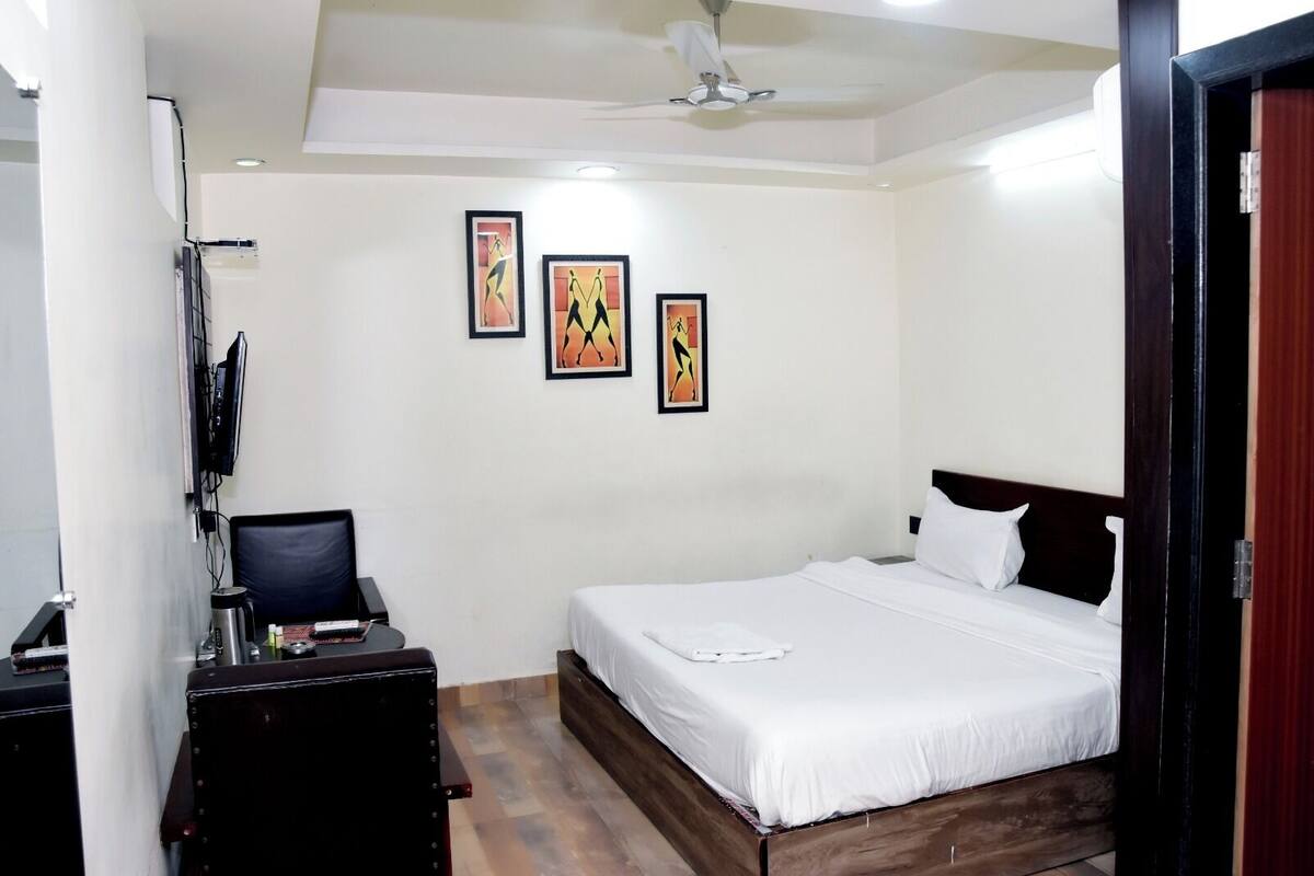 A bedroom with a bed, a desk, a chair, a TV, and three framed artworks on the wall.